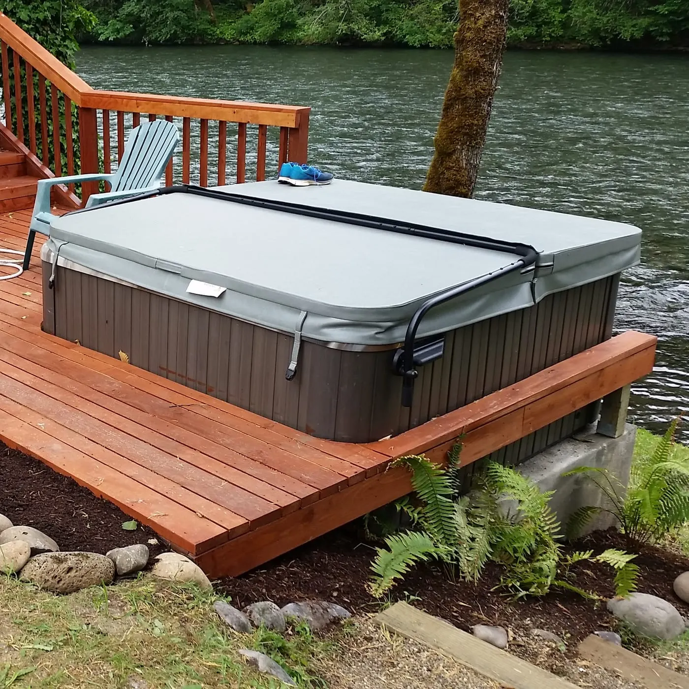 Red-brown composite deck with hot tub, chairs, and riverside view