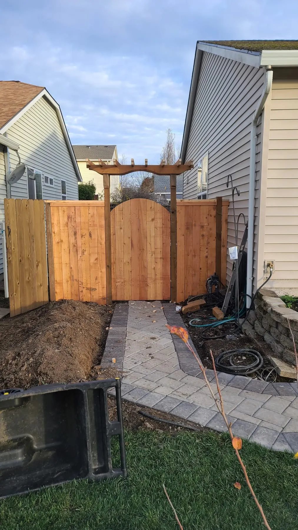 New cedar fence with arched gate and pergola arbor over a paver walkway