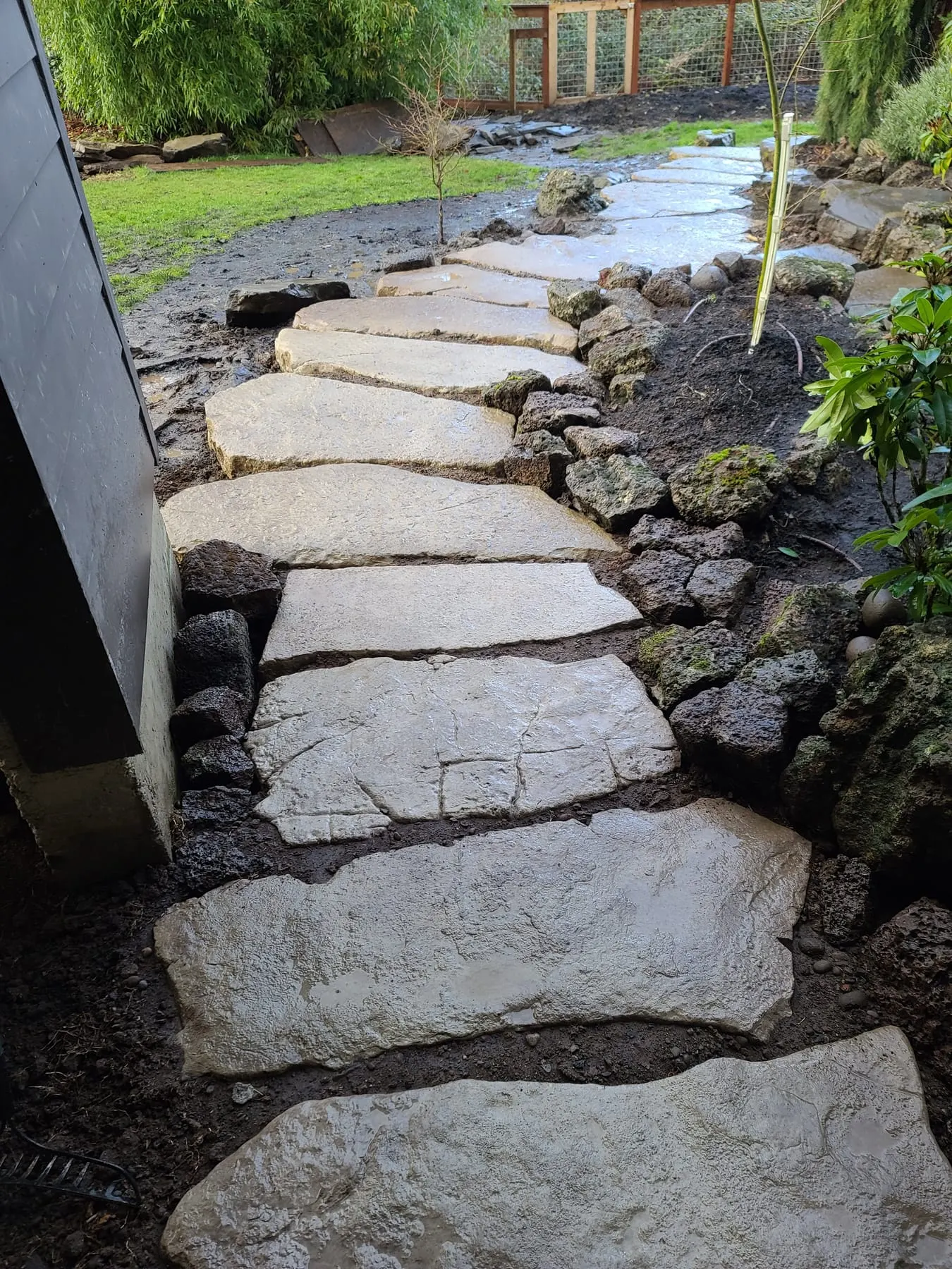Curved flagstone stepping path bordered by dark boulders through garden bed