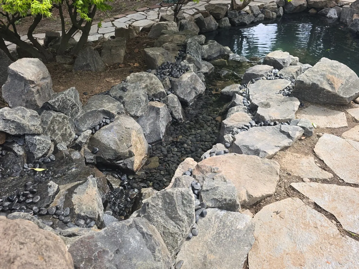 Boulder-edged pond with clear water and mature landscaping trees