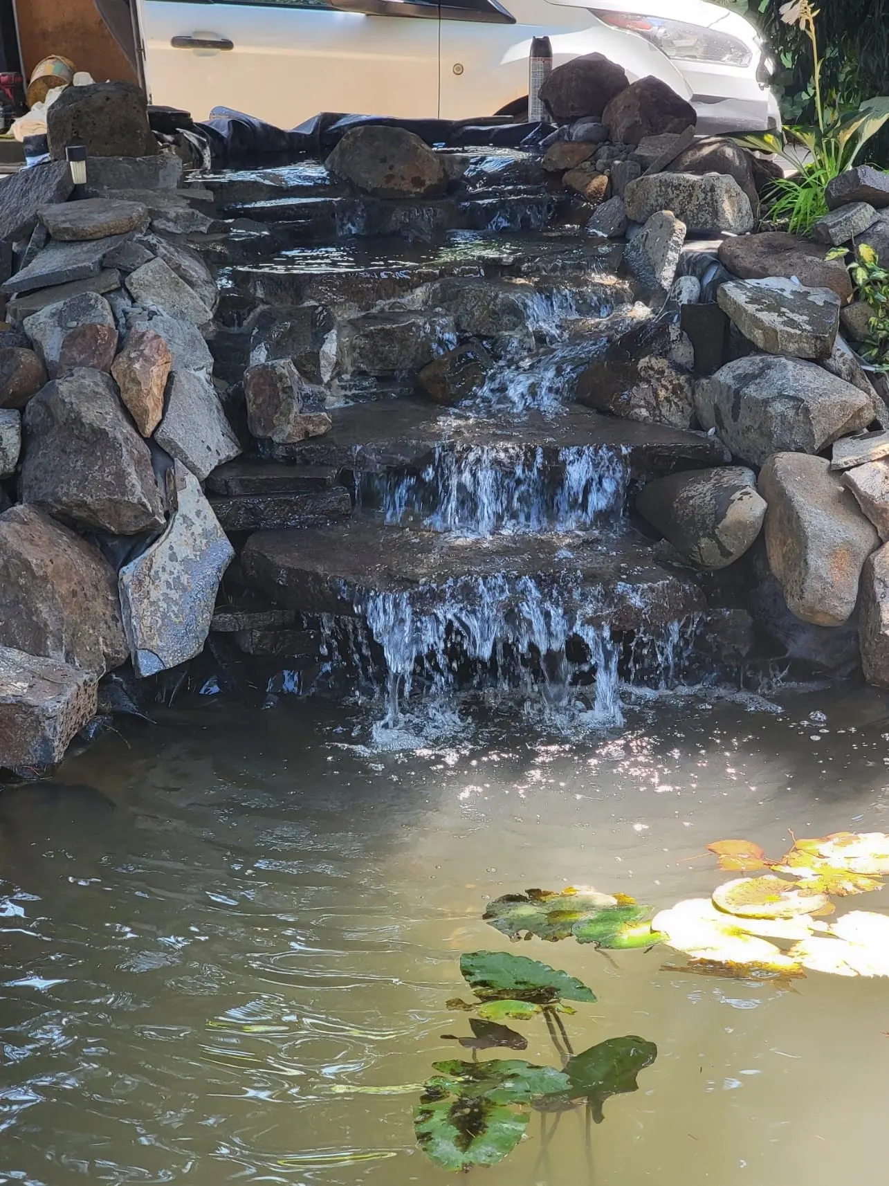 Multi-level stone waterfall cascading into pond with koi fish