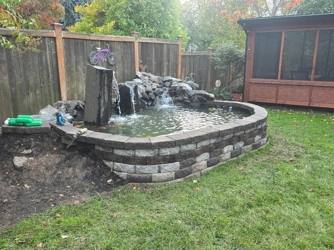 Curved stone-lined pond with waterfall and landscaping rocks in residential yard