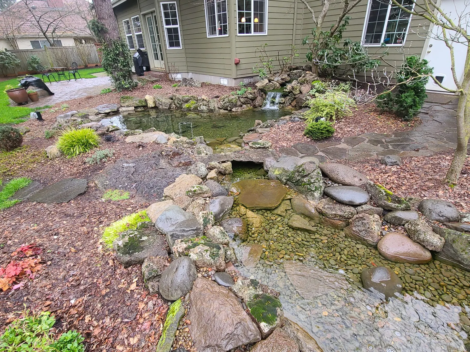 Established backyard pond with large boulders, green water, and surrounding landscape