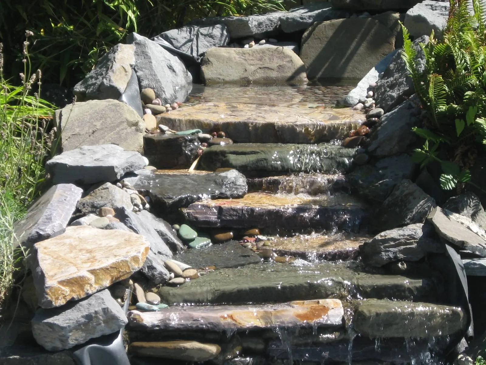 Multi-tiered stream with stacked stone steps and flowing water through landscaped channel