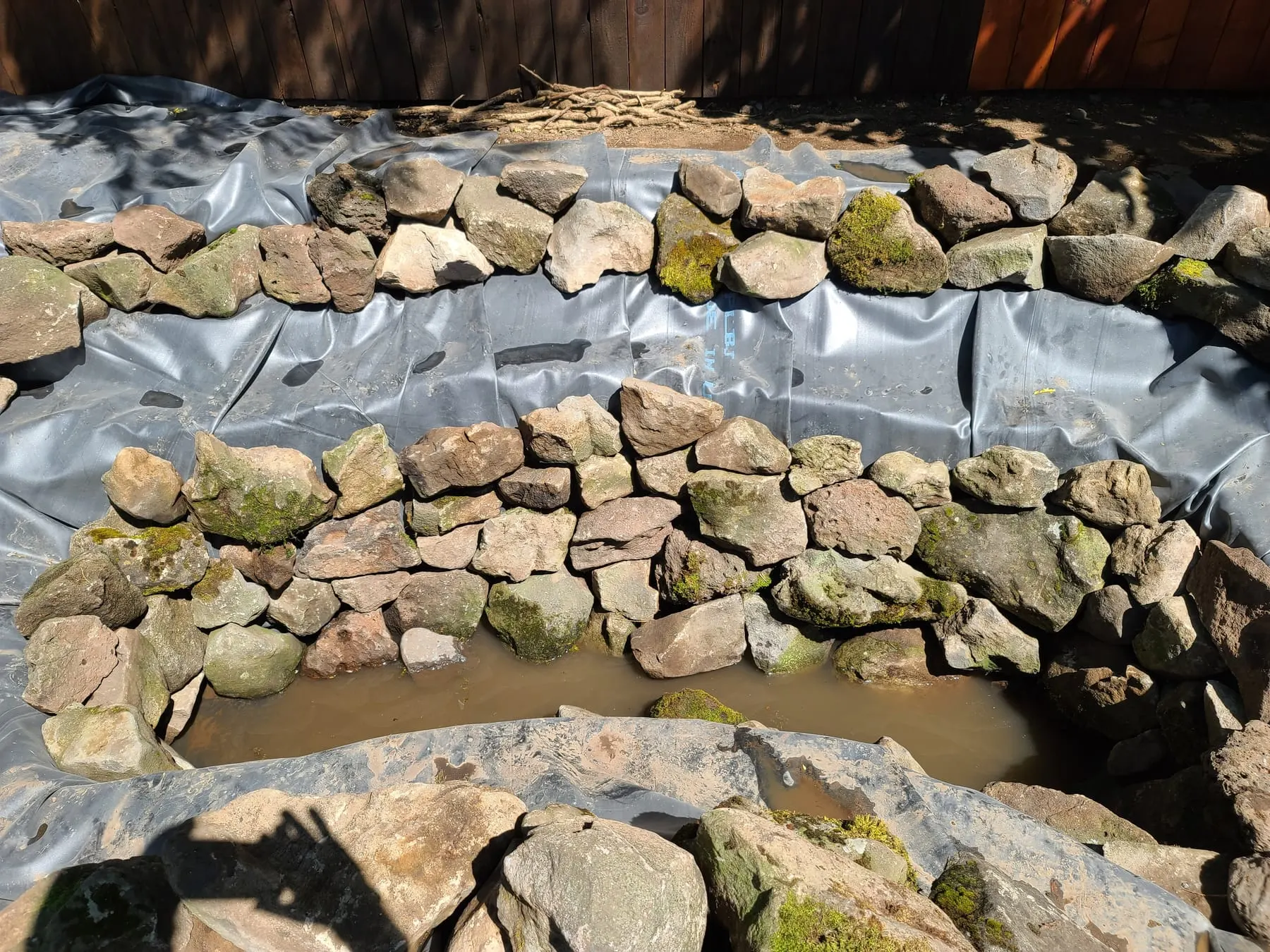 Pond under construction with stacked stone retaining walls and pond liner