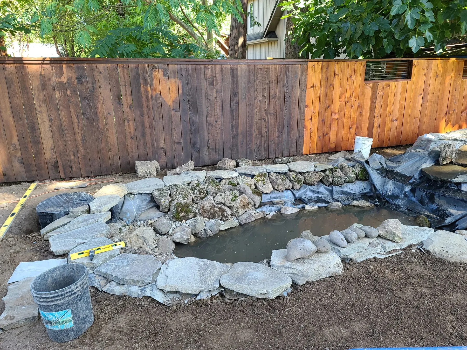 Half-built pond with stone lining and protective barrier, construction materials visible