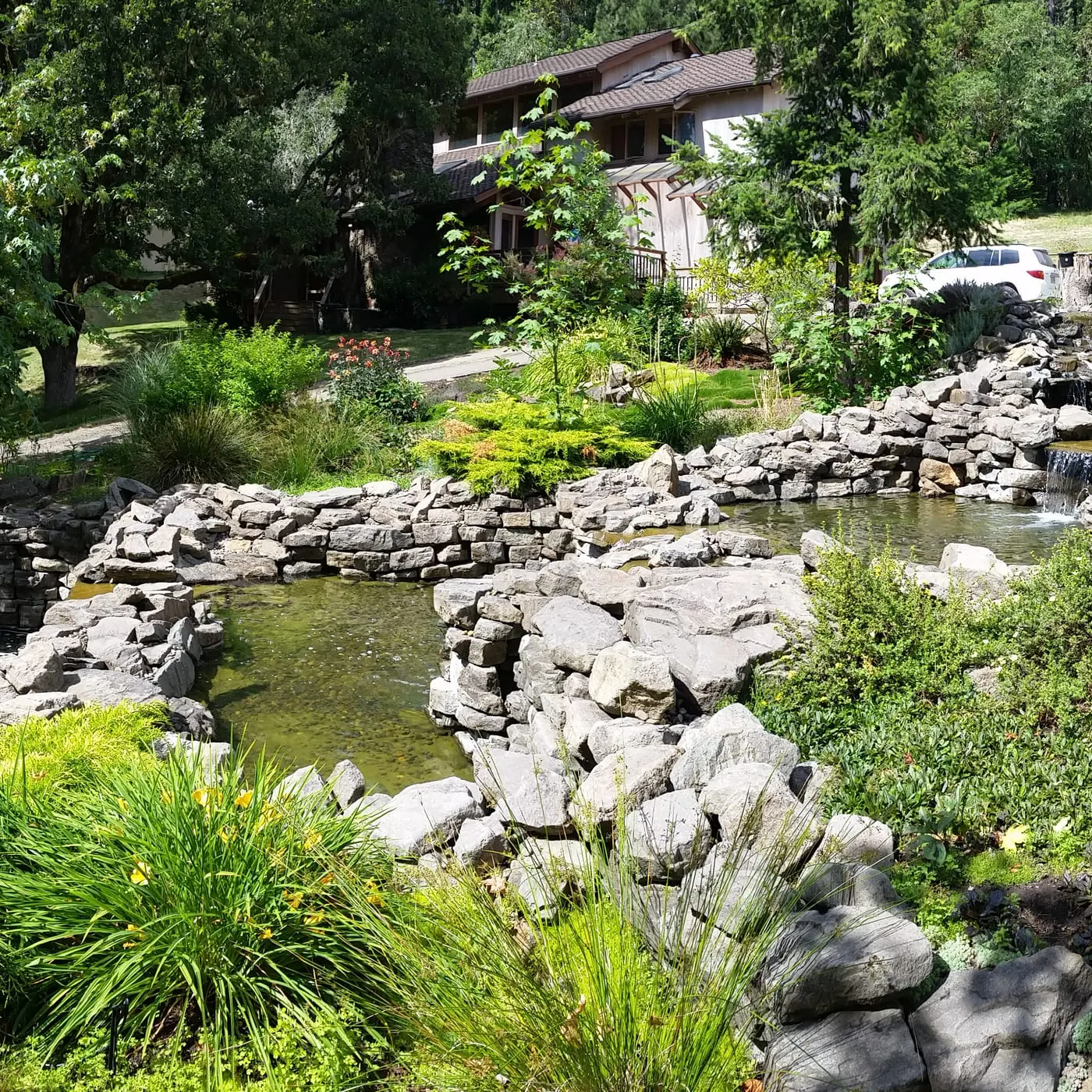 Multi-level pond with large boulders, ornamental grasses, and mature trees