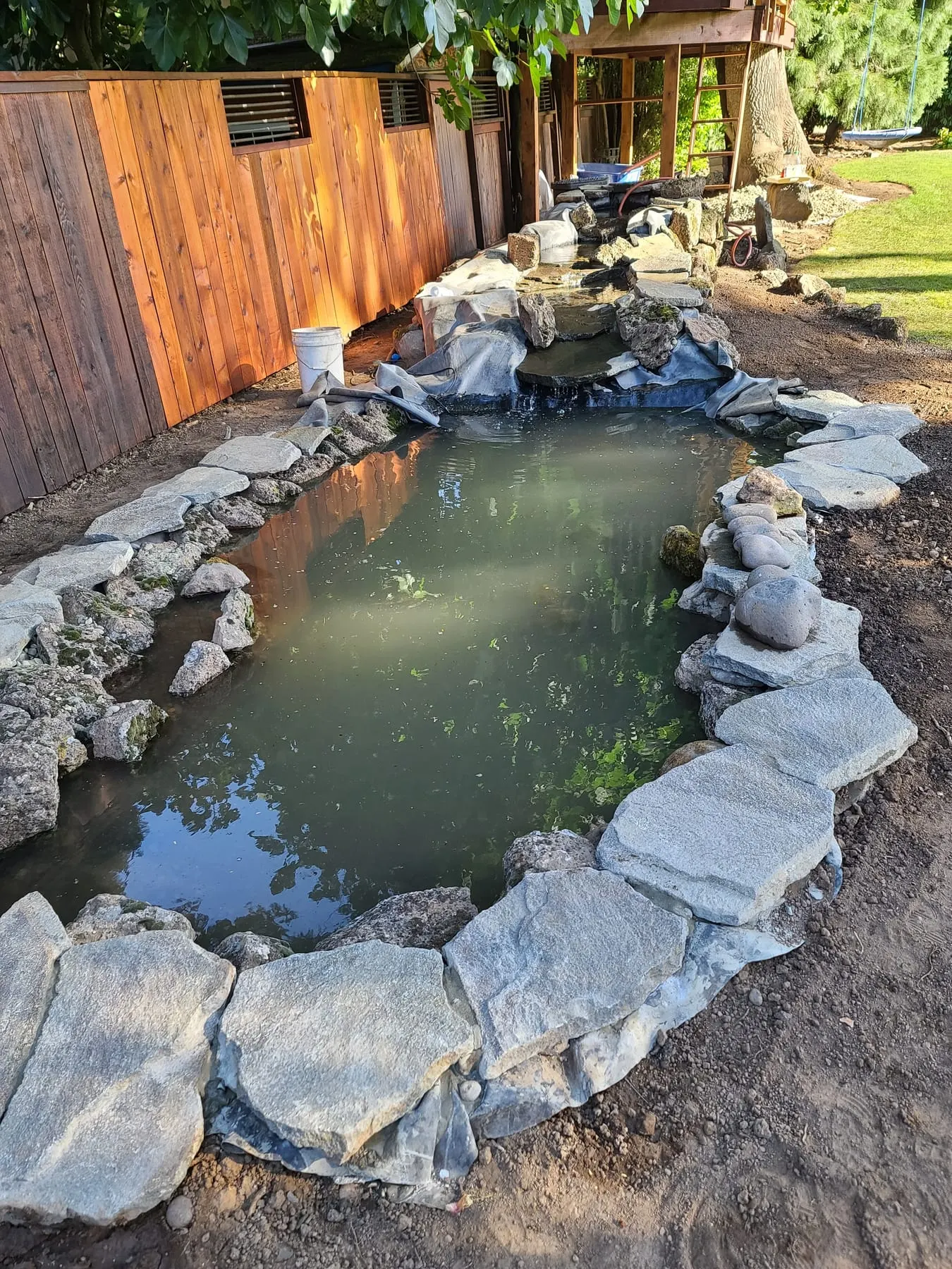 Backyard pond with stone edging and construction materials nearby